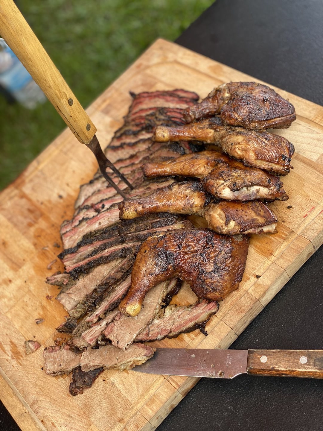 Leg quarters and brisket on wood cutting board with knife.