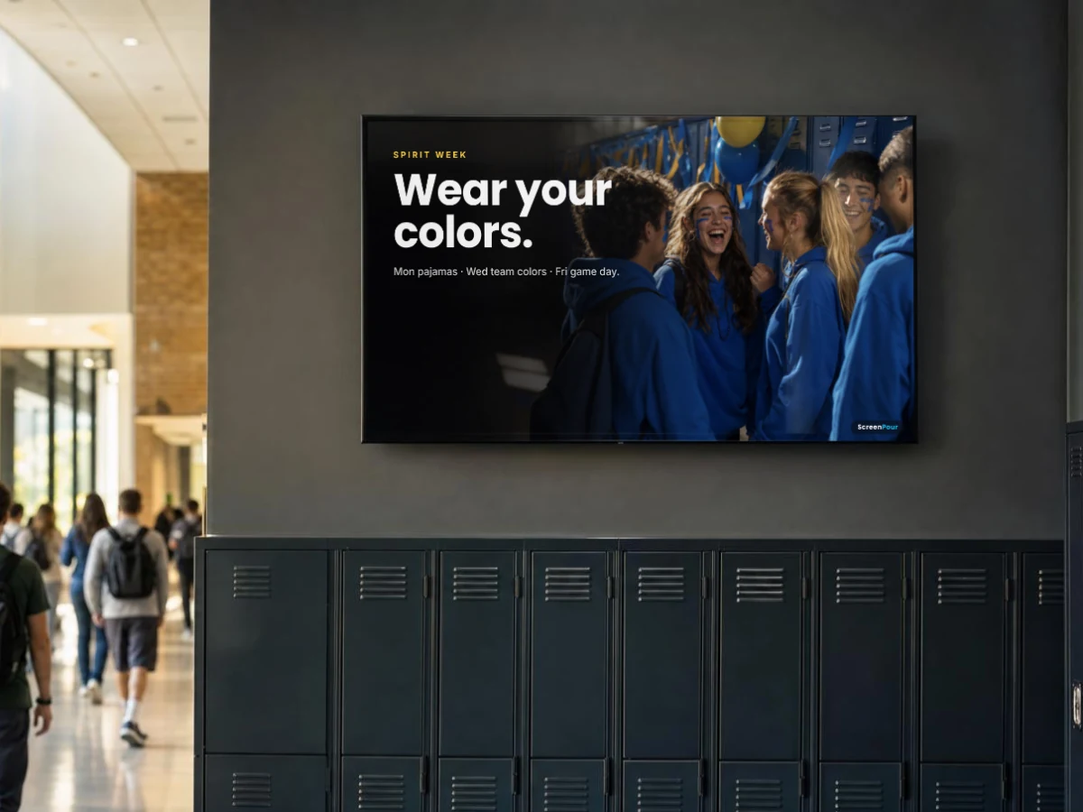 A screen above school hallway lockers announcing spirit week over a photo of students in team colors